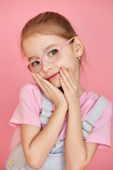 Adorable girl in pink glasses and denim overalls poses on pastel background. Cute child portrait shows confidence and playful elegance.
Soft light highlights innocence, charm, and modern style.
