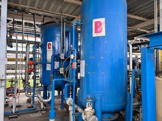 Industrial water treatment plant interior with rows of large blue filtration tanks, complex piping, valves, and control gauges for water purification and chemical processing.