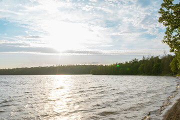 Serene nature landscape featuring calm lake, green forest, and pastel sunset sky.