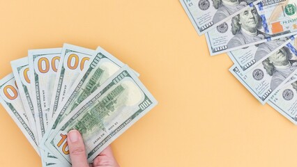 Money Matters Hand Holding 100 Bills and Scattered Cash on Solid Background, Investment Concept