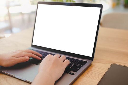 A person's hands typing on a laptop with a blank white screen in a bright, modern office or cafe. A versatile mockup for remote work, business, or education. - Powered by Adobe