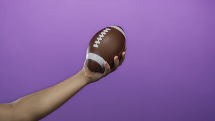 Man holding football in hand against a vibrant purple background, showcasing male grip and sports equipment for athletic themes in a minimalist isolated setting. - Powered by Adobe