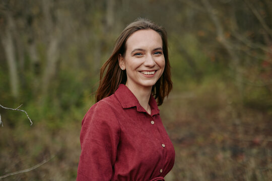 Candid outdoor portrait of a smiling young woman in a red shirt, natural expression, soft lighting and relaxed posture conveying authenticity and trustworthiness for genuine lifestyle imagery.