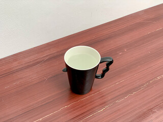 A modern black mug with an ergonomic handle, filled with clear water, resting on a reddish-brown wooden surface.
