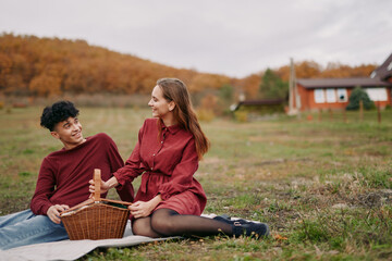 A genuine candid picnic scene of a young couple sharing a wicker basket on a blanket in the countryside, natural interaction and truthful emotional expression reflecting authenticity and accuracy.
