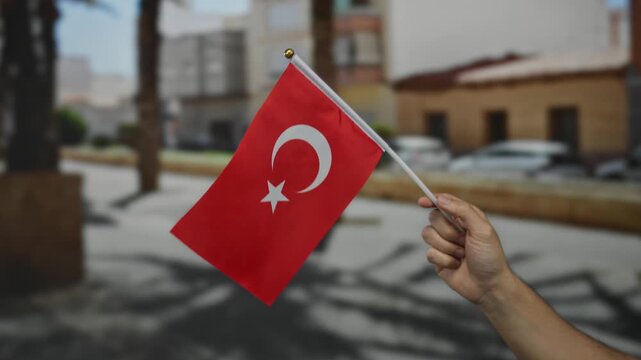 Man holding turkish flag outdoors on a sunny city street, capturing national pride and cultural identity in an urban setting.