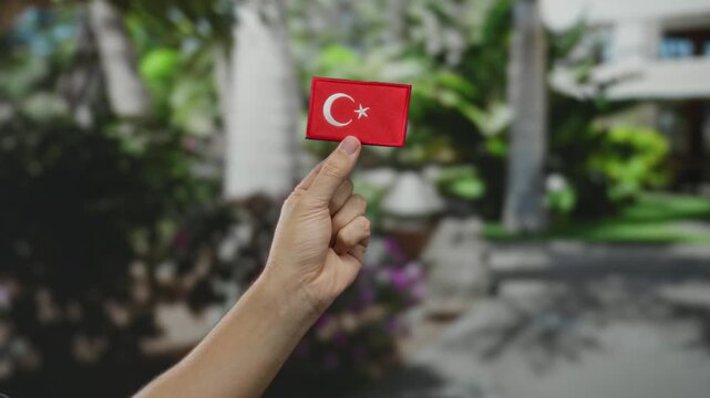 Man holding turkish flag patch outdoors in sunny park showing strong national pride with blurred greenery enhancing focus on hand gesture and cultural symbol in natural environment.