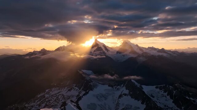 Majestic aerial drone shot slowly reveals a vast mountain range as golden sun rays break through dramatic clouds at sunset, illuminating peaks peaks, exploration, rugged