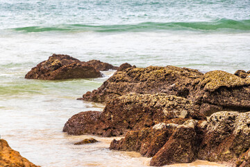 Rocky beach with rocks waves turquoise water in Patong Thailand.