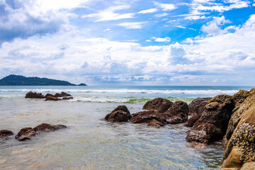 Rocky beach with rocks waves turquoise water in Patong Thailand.