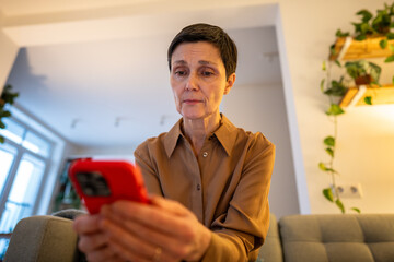 Mature woman scrolls endlessly in smartphone lost in digital distraction at home, scrolling...