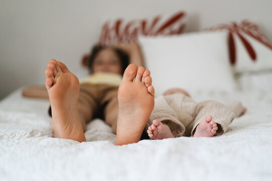 Two pairs of feet two little boys brothers rest on a soft, white bedspread, symbolizing connection and joy in family life. Moments of relaxation are shared between family members at home. - Powered by Adobe