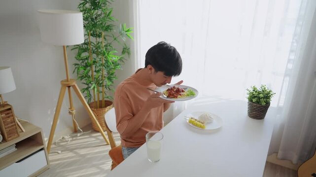 Asian handsome young man eating spaghetti and dimsum in kitchen at home.