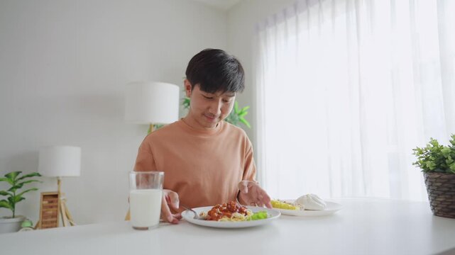Asian handsome young man eating spaghetti and dimsum in kitchen at home.