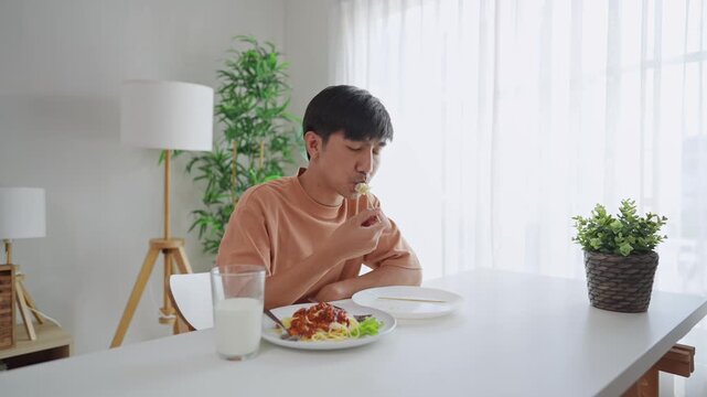 Asian handsome young man eating spaghetti and dimsum in kitchen at home.