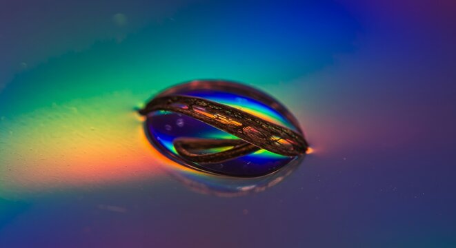 Close-up of a rainbow-colored water droplet on a reflective surface with vibrant iridescent rainbow hues and smooth gradient background in fascinating macro photography style