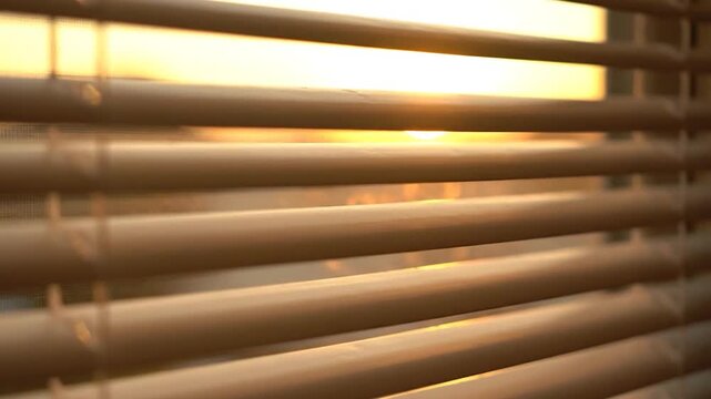 A close-up view of wooden blinds partially obscuring a bright, golden sunset in the background