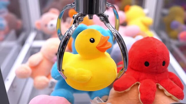 Bright yellow rubber duck toy captured by a claw machine in a game arcade.