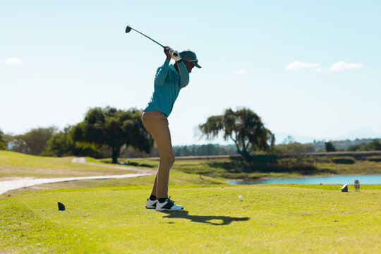 African American man takes golf shot on grassy course
