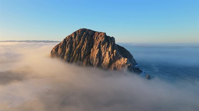 Breathtaking aerial views of a rugged rocky emerge above the mist, beautifully capturing the serene and tranquil beauty of natures various coastal landscapes. Morro Bay Rock , California, USA