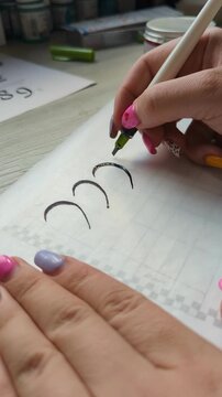 Detailed view of a calligraphy process with ink pen and artist hand. Paper, handwriting, and artistic composition merge in creative lettering practice. Female hand of artist.
