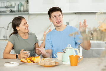 Happy young couple sitting at the kitchen-table and having a warm conversation while drinking tea