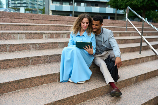 Diverse business people using tablet sitting on stairs