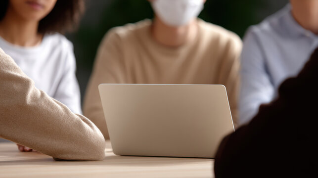 Group of people with visible lower faces sitting around table with laptop discussing health and safety