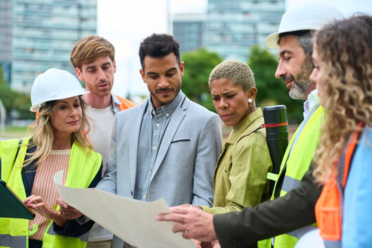 Diverse construction team reviewing blueprint on site