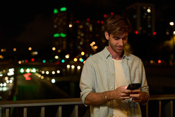 Young man smiling while using smartphone at night