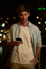 Young man smiling and using smartphone at night