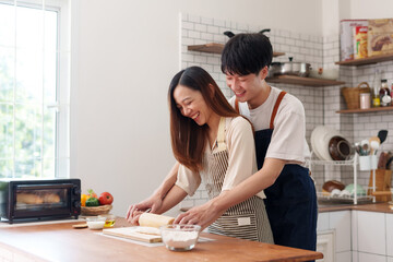 Happy young couple baking homemade bread, rolling dough, and smiling while enjoying time together in a bright kitchen