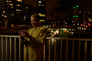 Woman smiling using smartphone on urban bridge at night