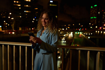 Woman using smartphone on bridge at night