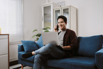 Smiling man relaxing on a couch, multitasking with a laptop and phone, enjoying remote freelance work