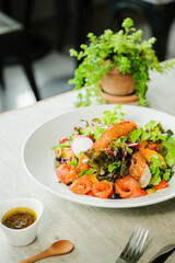 Delicious Salmon Salad on a table setting. A fresh bowl of salmon salad is beautifully presented on a table, accompanied by a small bowl of dressing and a wooden spoon.
