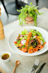 Fresh and healthy salad in a white bowl with wooden spoon and fork on a table.