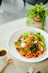A vibrant and fresh salad in a bowl, set on a wooden table, next to small decorative plant.