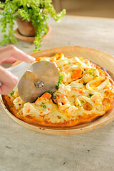 A seafood pizza being sliced with a cutter, ready to be served and enjoyed