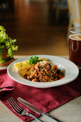 A plate of delicious spaghetti bolognese with a side of garlic bread and a glass of beer, ready to be enjoyed