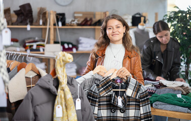 Young woman buyer choosing warm checkered coat in clothing store