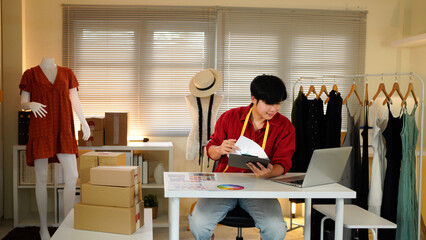 Male tailor work on items design with sketches, using laptop to review material and custom made sizes. Male professional tailor creating luxury clothes in workshop atelier