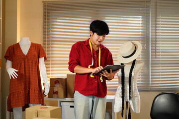 Male tailor work on items design with sketches, using laptop to review material and custom made sizes. Male professional tailor creating luxury clothes in workshop atelier