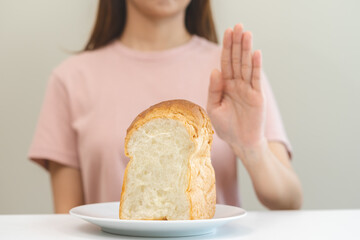 Gluten allergy, asian young woman hand push out, refusing to eat white bread loaf on plate in...