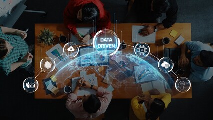 A group of diverse professionals collaborates around a table, engaging with digital data visuals and global network elements in a modern workspace environment. Raster