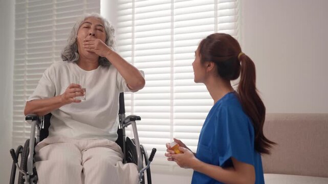 Asian senior woman wheelchair drinking water caregiver nurse assist taking medication elderly patient home healthcare support disabled mobility medical treatment well being assistance