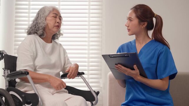 Asian elderly patient in wheelchair receives compassionate nursing care consultation from professional nurse in home environment addressing health concerns