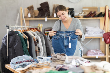 Uncertain young girl choosing jeans trousers in clothing shop with new winter collection