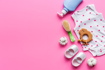 Set of baby hygiene cosmetic products - shampoo and soap with a comb. Eco friendly accessories - bodysuit and wooden toys with bottle of milk on pink background, top view