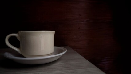 A photo of a coffee cup placed on a wooden table. The warm tones of the coffee and wood create a cozy and relaxing atmosphere. This image is perfect for themes related to morning routines, relaxation,
